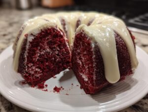 A moist red velvet bundt cake, sliced open to show the deep red crumb and topped with thick white cream cheese glaze.