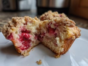 Close-up of a moist strawberry muffin cut in half, showing chunks of bright red strawberries inside and a streusel crumb topping.