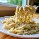 Close-up of fettuccine pasta coated in creamy Olive Garden Alfredo Sauce, lifted by a fork.