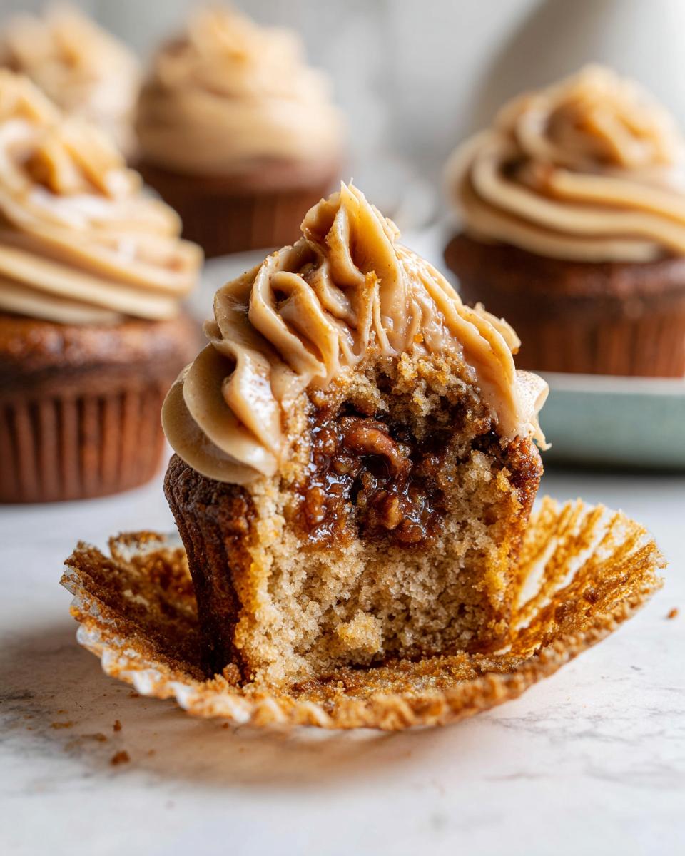 A close-up view of a pecan pie cupcakes cut in half, showing the gooey pecan filling and caramel-colored frosting.