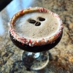 Top-down view of a peppermint espresso martini with a crushed candy cane rim and three coffee beans on the foam.