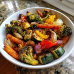 A white bowl filled with colorful, perfectly caramelized roasted vegetables, including broccoli, carrots, zucchini, and onions.
