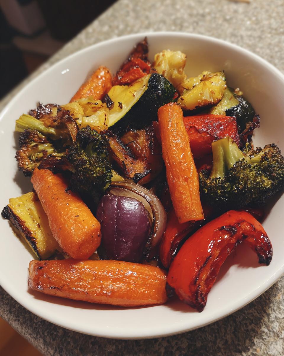 A white bowl filled with colorful, caramelized roasted vegetables, including carrots, broccoli, red onion, and peppers.