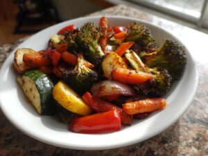 A white bowl filled with perfectly caramelized roasted vegetables, including broccoli, carrots, zucchini, and red peppers.