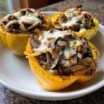 Three baked yellow bell peppers stuffed with steak, onions, and melted cheese, ready to eat philly cheesesteak stuffed peppers.