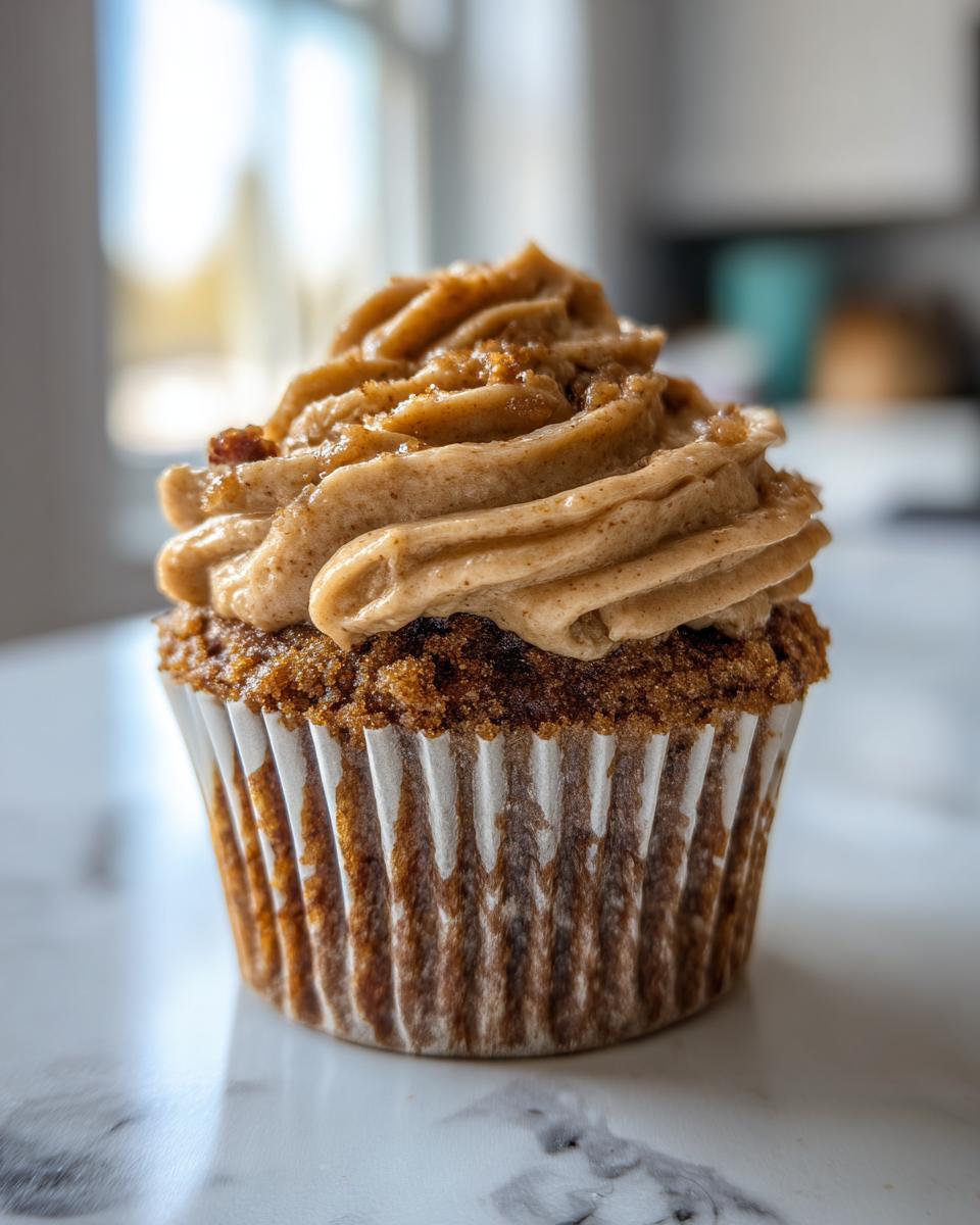 A close-up of a single pecan pie cupcake topped with thick, swirled brown sugar frosting.