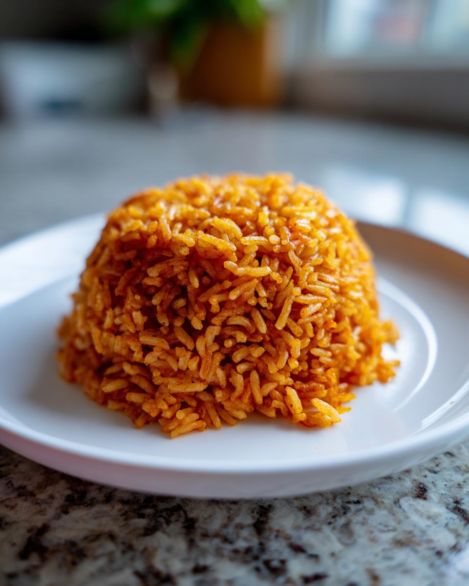 A mound of vibrant, orange-red smoky jollof rice served neatly on a white plate.