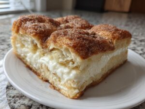 A thick slice of sopapilla cheesecake featuring a creamy white filling between layers of dough topped with cinnamon sugar.