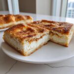 Two squares of creamy sopapilla cheesecake topped with cinnamon sugar, served on a white plate.