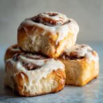 Close-up of three stacked, fluffy sourdough discard cinnamon rolls topped with thick white icing.