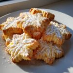 A pile of star-shaped italian butter cookies dusted generously with white powdered sugar on a white plate.