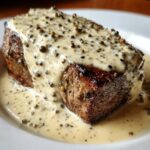 A perfectly cooked steak generously topped with rich, creamy peppercorn sauce and whole peppercorns.