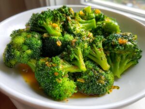 A close-up of vibrant green steamed broccoli florets coated in a savory, glossy sauce with visible garlic bits.