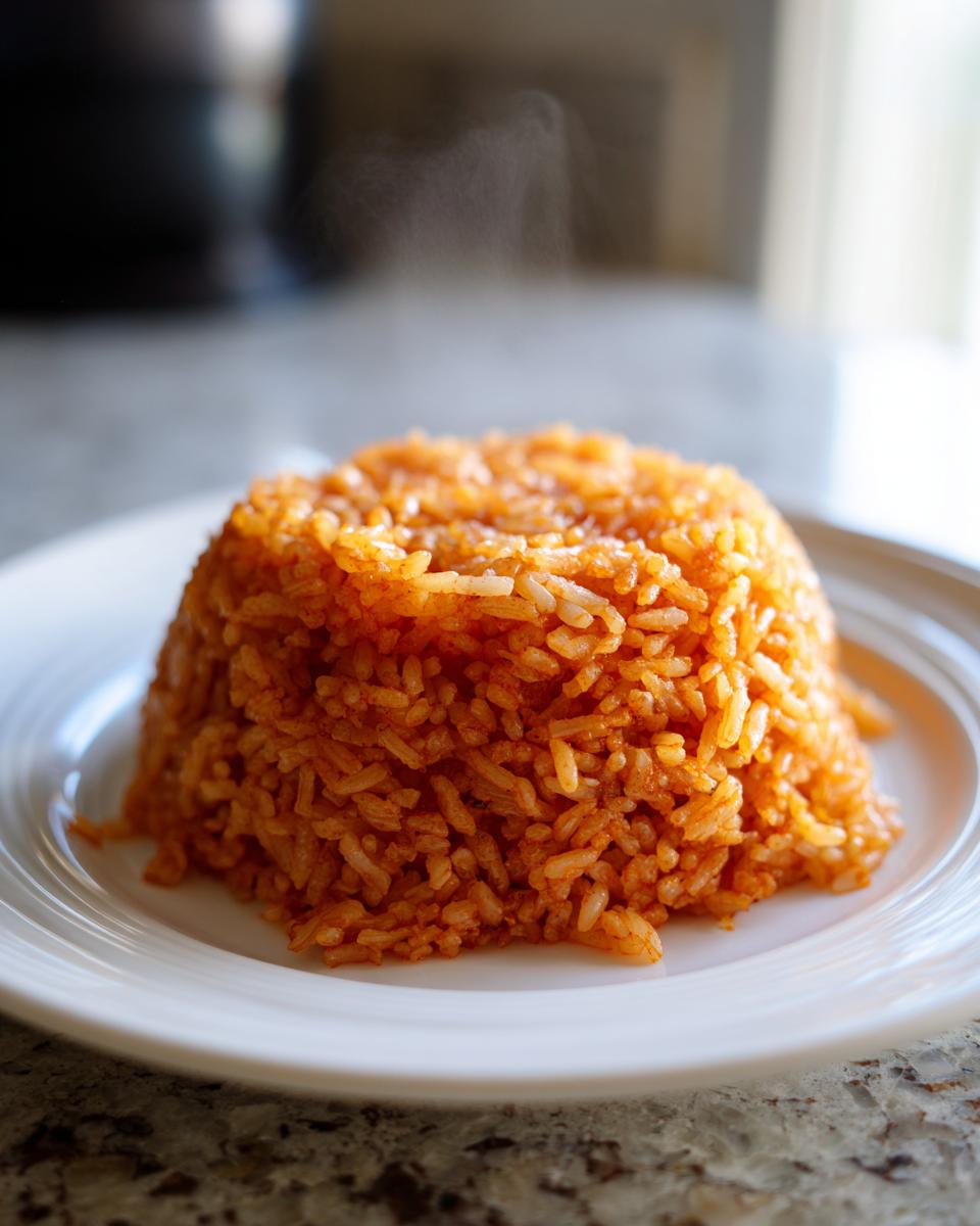 A perfectly molded, steaming mound of vibrant orange-red jollof rice served on a white plate.