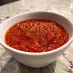 Close-up of a vibrant, chunky tomato sauce seasoned with herbs served in a small white bowl.