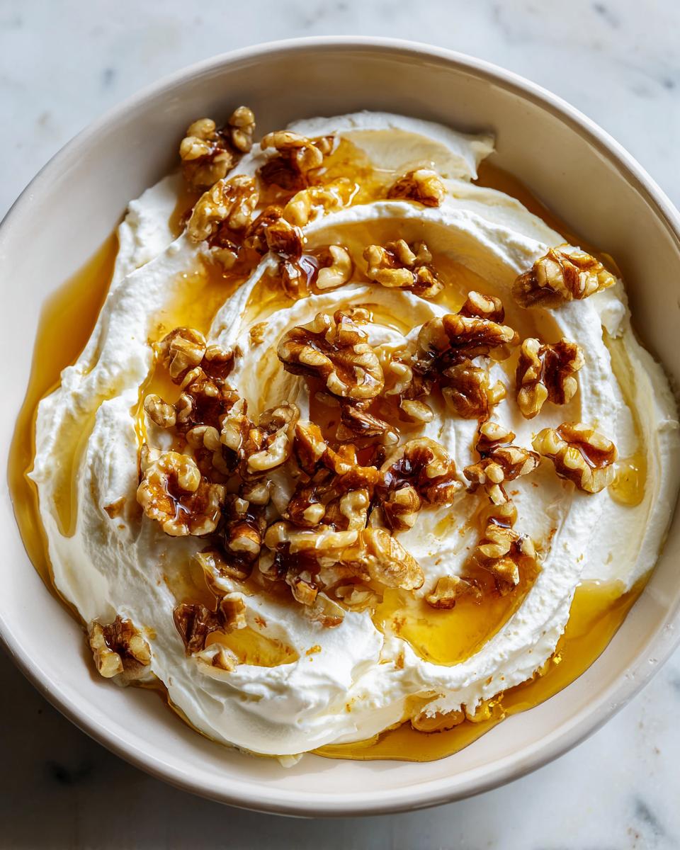 Close-up of a bowl containing creamy whipped ricotta dip, drizzled with honey and topped with candied walnuts.