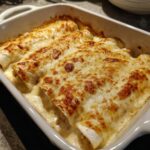 Close-up of three baked white chicken enchiladas covered in bubbly, browned cheese sauce in a white baking dish.