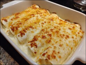 Close-up of creamy white chicken enchiladas baked in a white dish, topped with bubbling, browned cheese.