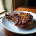 A close-up of a beautifully seasoned and crispy air fryer pork chops served on a white plate.