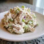 A scoop of creamy chicken salad mixed with diced green celery and red onion served on a white plate.