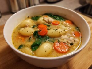 A white bowl filled with creamy, savory gnocchi soup featuring potato dumplings, sliced carrots, spinach, and shredded chicken.