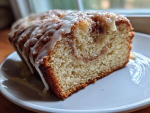 Close-up of a moist slice of apple fritter bread featuring a cinnamon swirl and drizzled with white vanilla glaze.