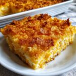 A close-up of a square slice of bright orange and white squash casserole topped with crispy, golden cornflakes.