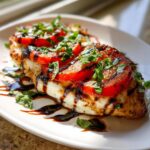 A grilled chicken breast topped with melted mozzarella, sliced tomatoes, and fresh basil, drizzled with balsamic glaze, representing caprese chicken.