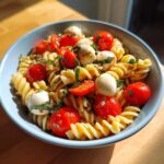 Close-up of a bowl of caprese pasta salad featuring fusilli, cherry tomatoes, mozzarella balls, and basil.