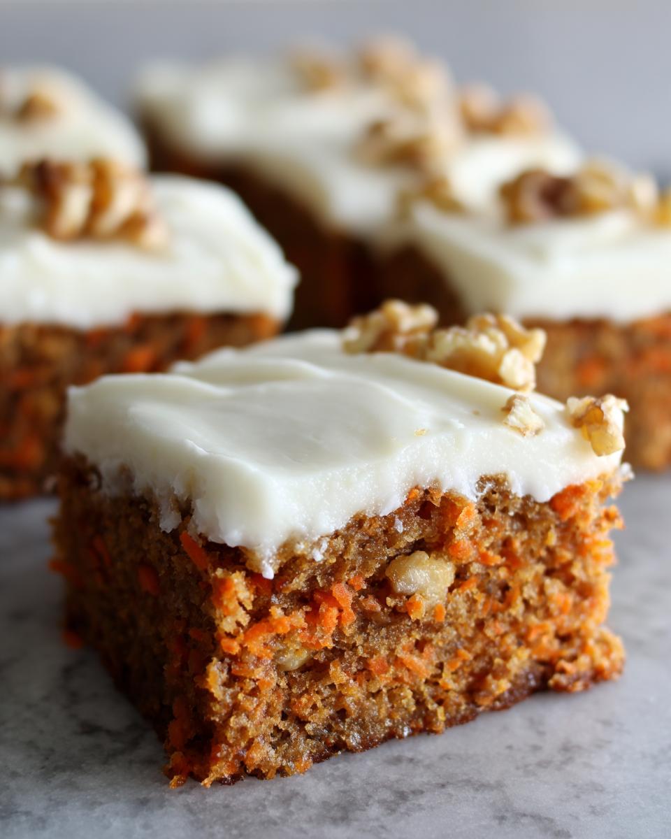 A close-up view of a square slice of moist carrot cake bars topped with thick cream cheese frosting and a walnut piece.
