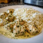 Close-up of juicy chicken scampi pieces in a creamy sauce served next to garlic parmesan rice.
