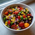 Close-up of vibrant Cowboy Caviar dip featuring black beans, corn, tomatoes, and onions in a white bowl.