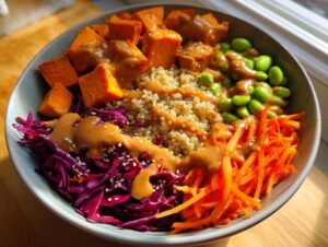 Close-up of a vibrant buddha bowl featuring quinoa, sweet potatoes, shredded carrots, red cabbage, edamame, and peanut sauce.