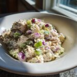 Close-up of creamy cottage cheese tuna salad mixed with chunks of red onion and celery in a white bowl.