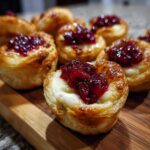Close-up of golden puff pastry cranberry brie bites topped with melted brie and rich cranberry sauce.
