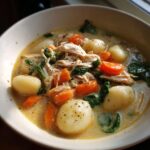 A close-up of a bowl of creamy chicken gnocchi soup, featuring soft gnocchi, shredded chicken, carrots, and spinach.