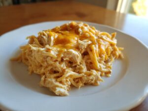 A generous serving of creamy chicken spaghetti topped with melted cheddar cheese on a white plate.