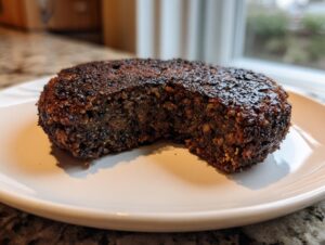 A perfectly seared, firm black bean burger resting on a white plate, showing its dense interior texture.