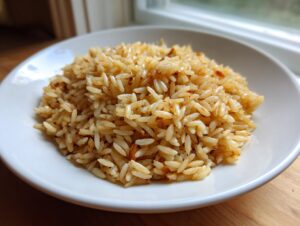 Close-up of fluffy, golden brown rice pilaf served in a white bowl near a window.