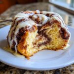 Close-up of a fluffy slice of cinnamon roll cake recipe, drizzled heavily with white icing.