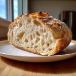 Cross-section of fluffy sourdough bread showing an open, airy crumb structure on a white plate.