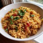 Close-up of fluffy spanish rice mixed with tomatoes and topped with fresh cilantro in a white bowl.