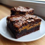 Close-up of a fudgy caramel brownie square with a gooey caramel layer and flaky sea salt.