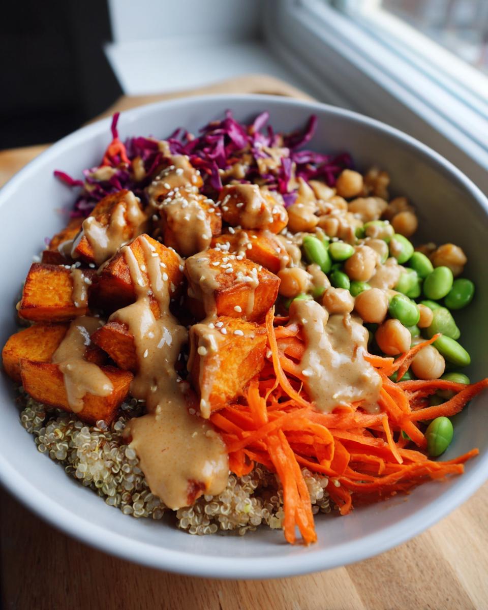 Close-up of a colorful buddha bowl featuring quinoa, roasted sweet potatoes, edamame, carrots, and peanut dressing.
