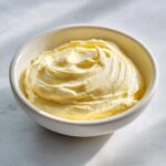 A close-up of thick, pale yellow homemade mayonnaise swirled beautifully in a small white bowl.