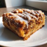 A close-up shot of a single serving of delicious apple pie bars topped with white vanilla icing.