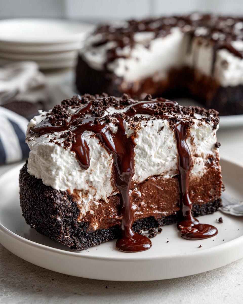 A close-up slice of Mississippi Mud Pie featuring a thick crust, chocolate filling, whipped topping, and rich chocolate syrup drizzle.