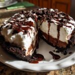 A decadent slice removed from a Mississippi Mud Pie, showing layers of chocolate filling and whipped cream topping drizzled with fudge.