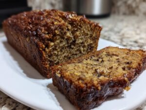 A close-up of a freshly baked, moist banana bread loaf with one slice cut and resting beside it.