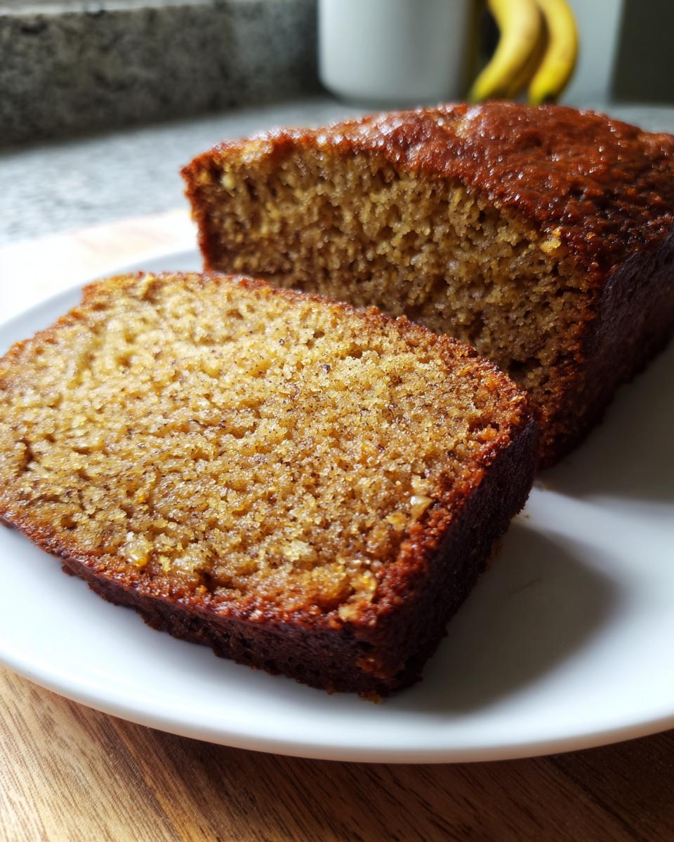 Close-up of a moist slice of banana bread recipe loaf on a white plate, showing a sugary crust.